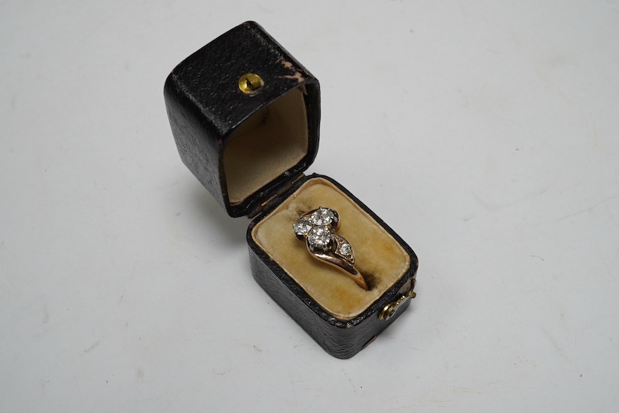 A yellow metal and three stone diamond set crossover ring, with single stone diamond set shoulder, size K, gross weight 2.4 grams. Condition - poor to fair